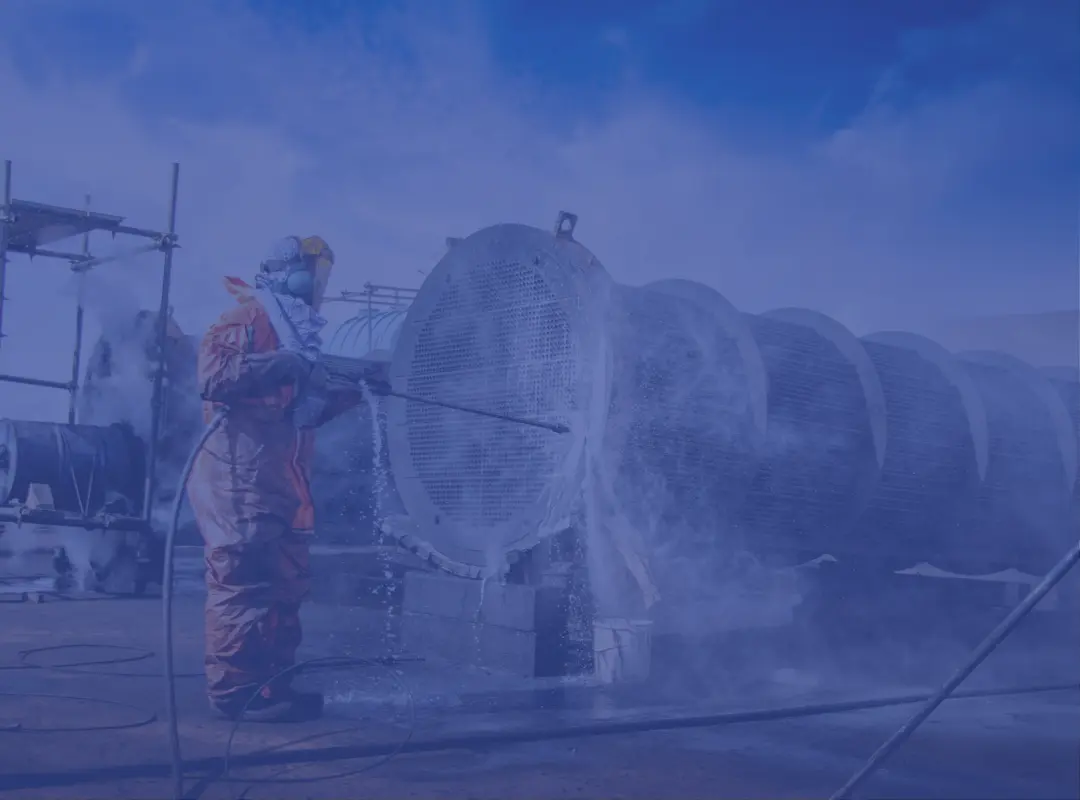 Tube bundle cleaning with high pressure water jetting under a cloudy blue sky.